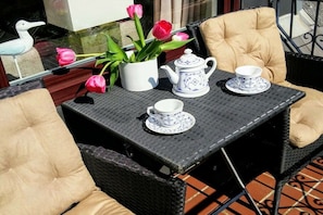 Un'area esterna con sedute in vimini, un tavolo con teiera e tazze, e un vaso con tulipani rosa.