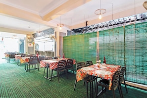 Interior de restaurante com mesas, cadeiras, parede texturizada verde e luminárias pendentes.