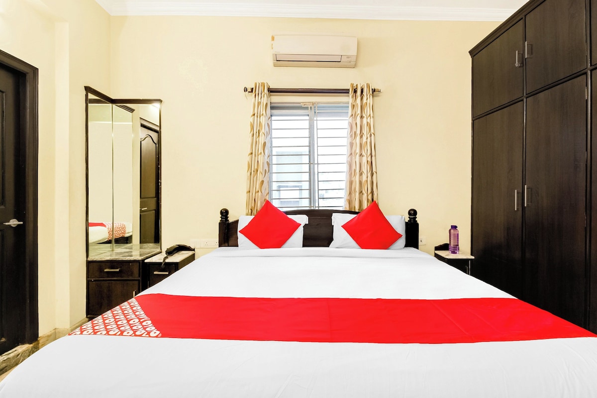 Quarto de hotel com cama, mesa de cabeceira, espelho, guarda-roupa e janela com cortinas.
