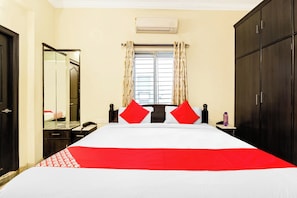 Quarto de hotel com cama, mesa de cabeceira, espelho, guarda-roupa e janela com cortinas.