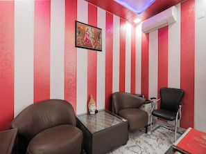 Una habitación con paredes a rayas, una estatua de Buda, dos sillones de cuero, una mesa de centro de vidrio y un libro rojo sobre una mesa.