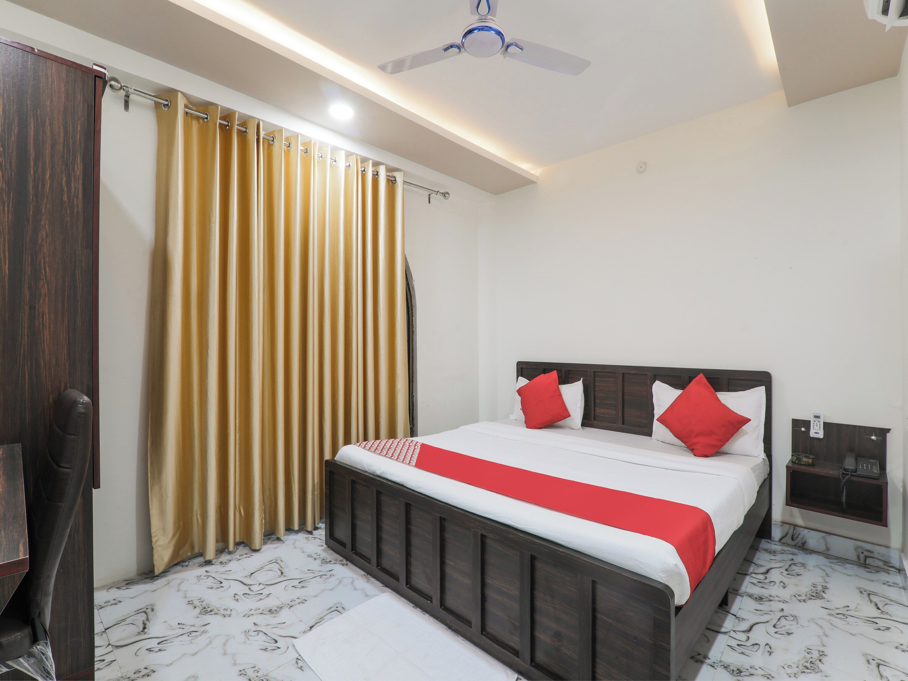 Una habitación de hotel con una cama, cortinas, un ventilador de techo y una mesita de noche con un teléfono.