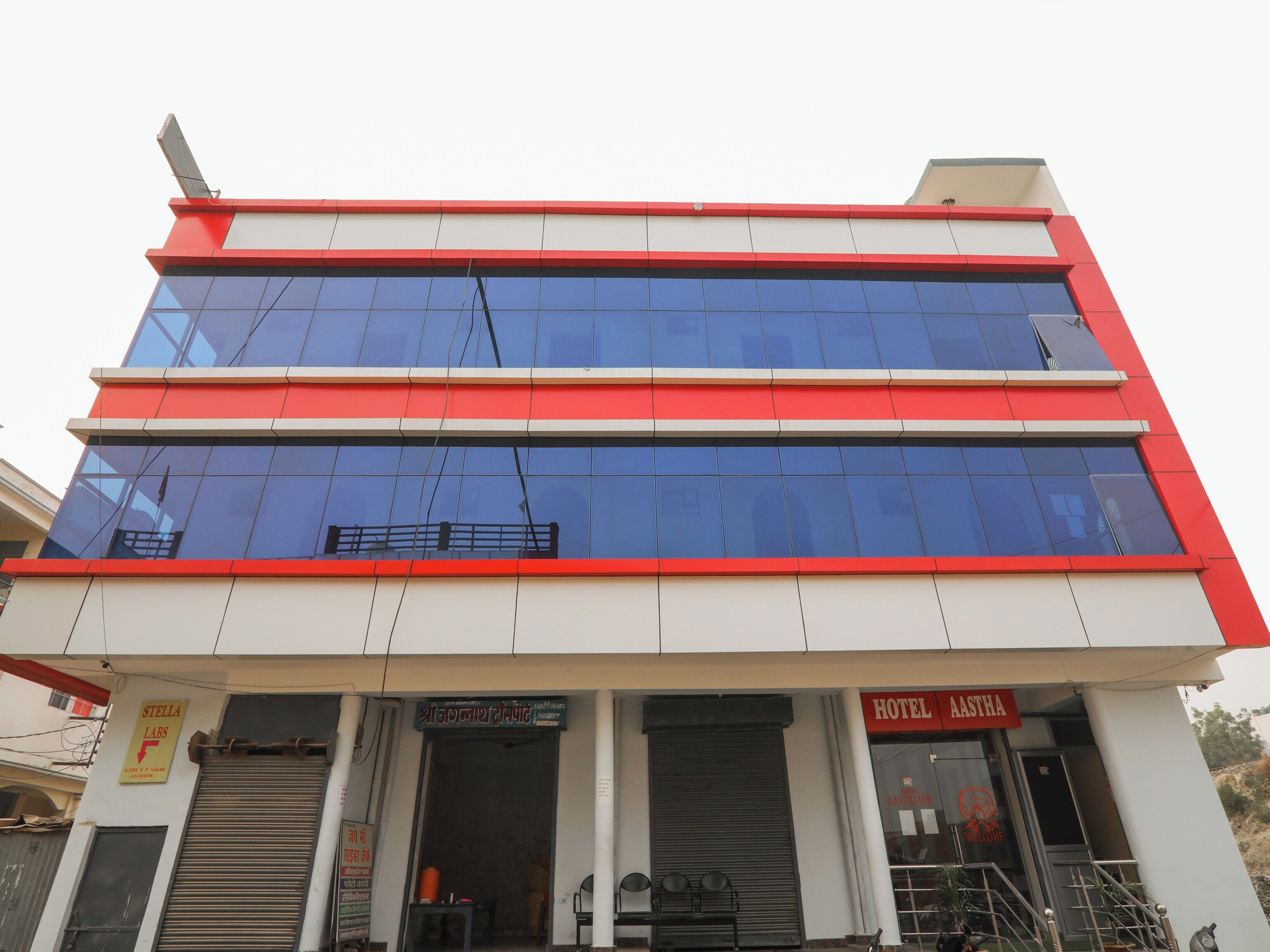 Un edificio de varios pisos con fachada roja y blanca, que incluye un letrero de 'Stella Labs' y la entrada del 'Hotel Rastha'.