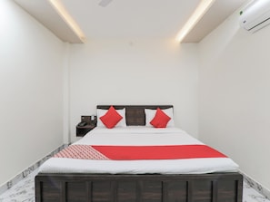 Una habitación de hotel con cama, mesita de noche y equipo de aire acondicionado.