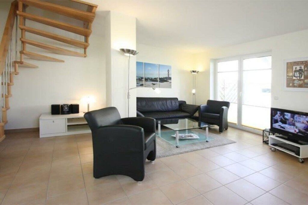 A modern living room with a staircase, a sofa set, a coffee table, a television, and a large window.
