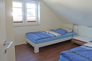 A single-bed room with a sloped ceiling, a window with blinds, a bedside table, and a door. - Holiday apartment "Hanne-Hus" 322225 (Kühlungsborn)