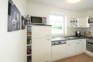 A compact kitchen with white cabinets, a microwave, a sink, and a window providing natural light. - Holiday apartment "Hanne-Hus" 322225 (Kühlungsborn)