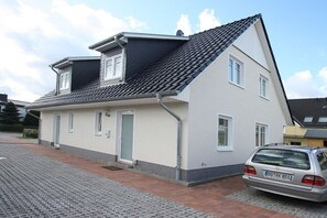 A two-story house with a tiled roof, a car parked in the driveway, and a paved walkway. - Holiday apartment "Hanne-Hus" 322225 (Kühlungsborn)