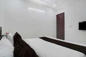 A hotel room with a single bed, a flat-screen TV mounted on the wall, and a door with a handle. - Townhouse Sector 46 Huda Market (Gurugram)