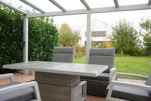 A covered patio area with a table and chairs, surrounded by greenery. - Holiday home in Schweich with swimming pool (Schweich)