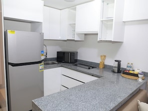 A compact kitchen with white cabinets, a stainless steel refrigerator, a microwave, and a granite countertop. - Your Dream Studio in New Cairo E104, AC, Wi-Fi, Prime Location (Cairo Governorate)
