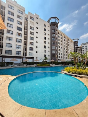 A swimming pool surrounded by a hotel building with multiple floors and balconies. - Your Dream Studio in New Cairo E104, AC, Wi-Fi, Prime Location (Cairo Governorate)