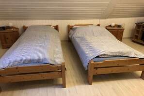 Twee houten bedden met geruit beddengoed in een kamer met houten vloeren en witte wanden.