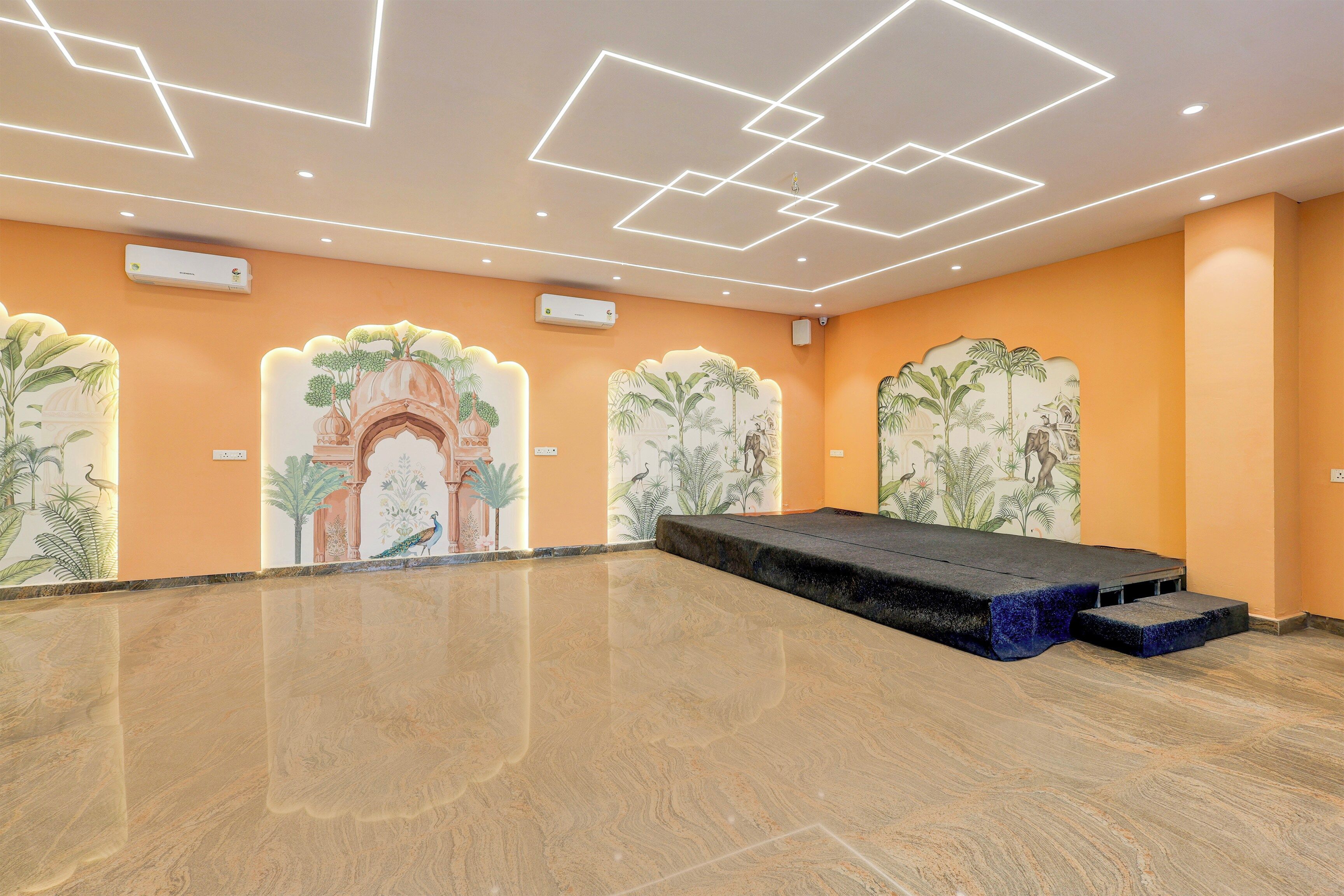 Una habitación amplia con escenario, murales decorativos e iluminación empotrada en el techo.