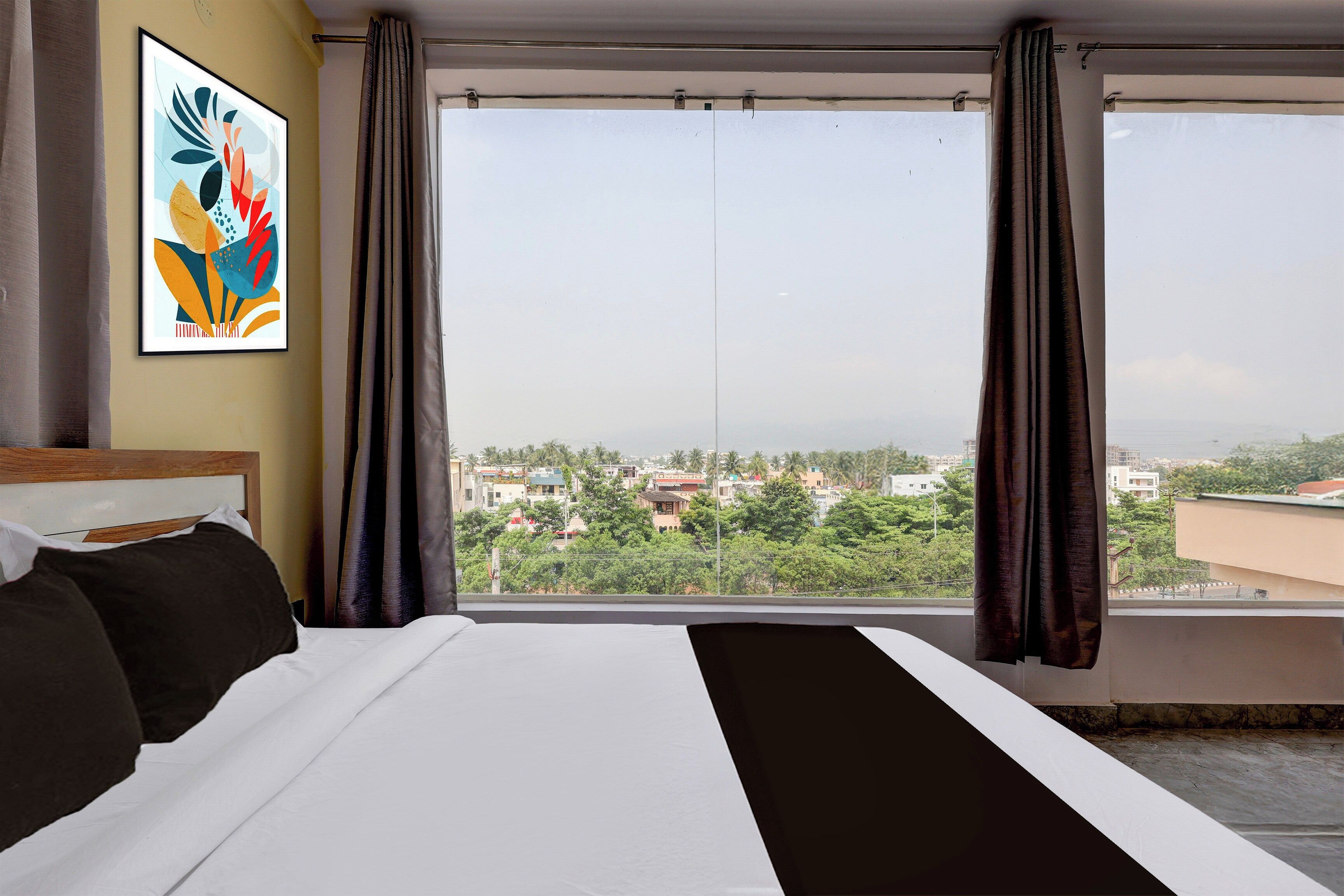 A hotel room with a large bed, a window with curtains, and a city view.
