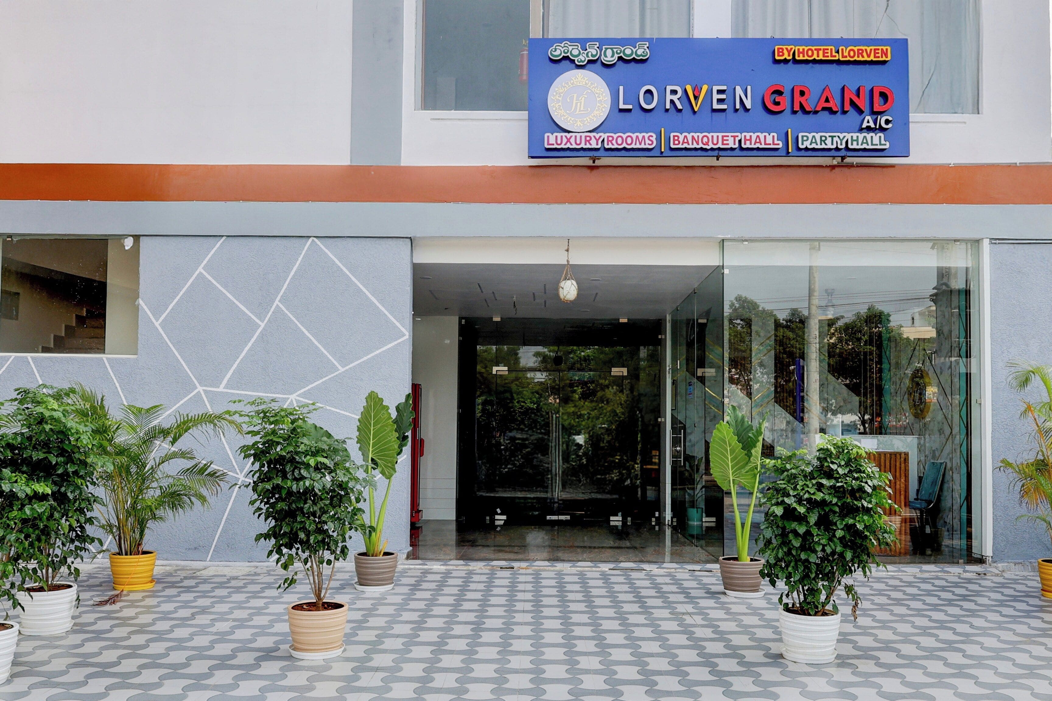 L’entrée d’un hôtel, avec une enseigne indiquant « Lorven Grand A/C », signalant la présence de chambres de luxe, d’une salle de banquet et d’une salle de réception.