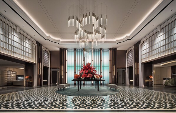 A spacious lobby with a modern chandelier, a central floral arrangement, and a patterned floor.