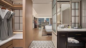 Une chambre d’hôtel moderne dotée d’un grand lit, d’une salle de bain avec un miroir et un lavabo, et offrant une vue sur le paysage urbain.