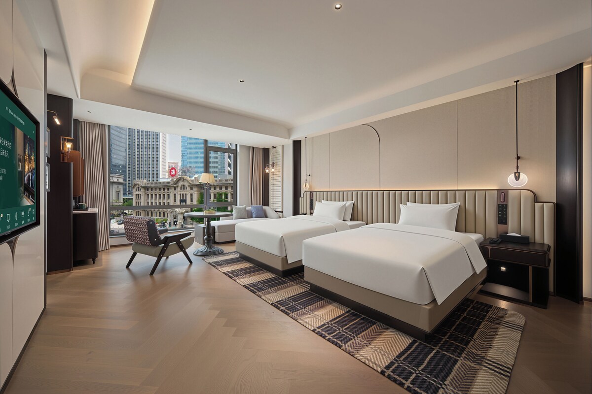 Une chambre d’hôtel moderne avec deux lits, un bureau et une vue sur le paysage urbain.