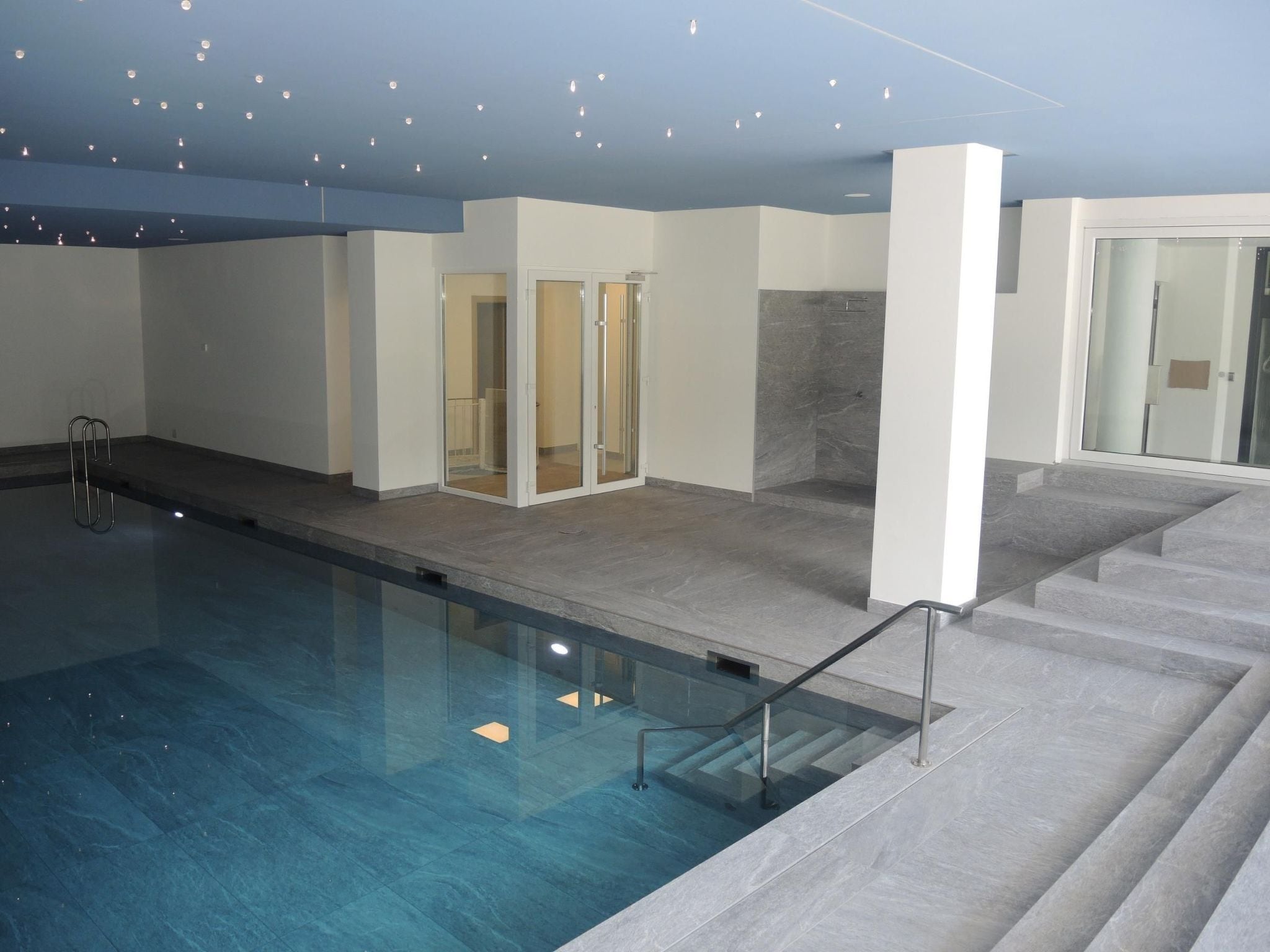 A swimming pool with a glass barrier, a shower area, and a staircase leading to an upper level.