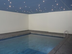 Una piscina con superficie de agua azul cristalina, rodeada de paredes y un techo con luces uniformemente distribuidas.