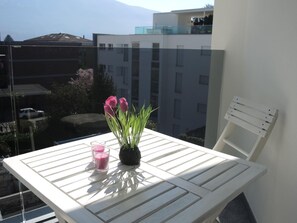 A balcony with a white table, a potted plant with pink flowers, and two glasses of pink liquid. - Fiore Rosa by Interhome (Ascona)