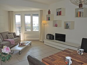 En moderne stue med sofa, sofabord, fjernsyn og bogreoler.