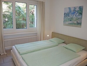 Et soveværelse med seng, radiator, et vindue med gardiner og et billede på væggen.
