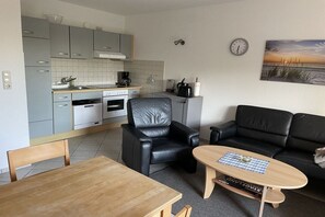A compact living space with a kitchenette, a dining table, a sofa, and a coffee machine. - Holiday apartment with 2 bedrooms (Heiligenhafen)