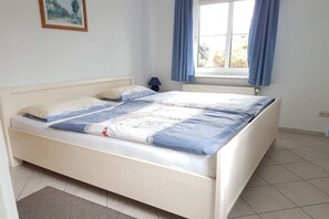 A bedroom with a bed, a nightstand, a window with curtains, and a radiator. - Holiday apartment with 2 bedrooms (Heiligenhafen)