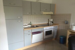 A compact kitchen with grey cabinets, a built-in oven, a coffee maker, and a trash bin. - Holiday apartment with 2 bedrooms (Heiligenhafen)