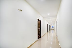 Un passadís llarg i ben il·luminat, amb portes a un costat i un senyal d'eixida d'incendis a la paret.