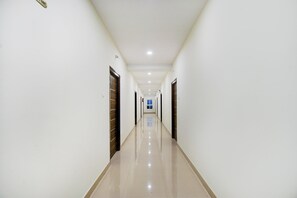 A long, narrow hallway with doors on both sides, leading to a bright room at the end. - Hotel O 4 COLORS (Hyderabad)