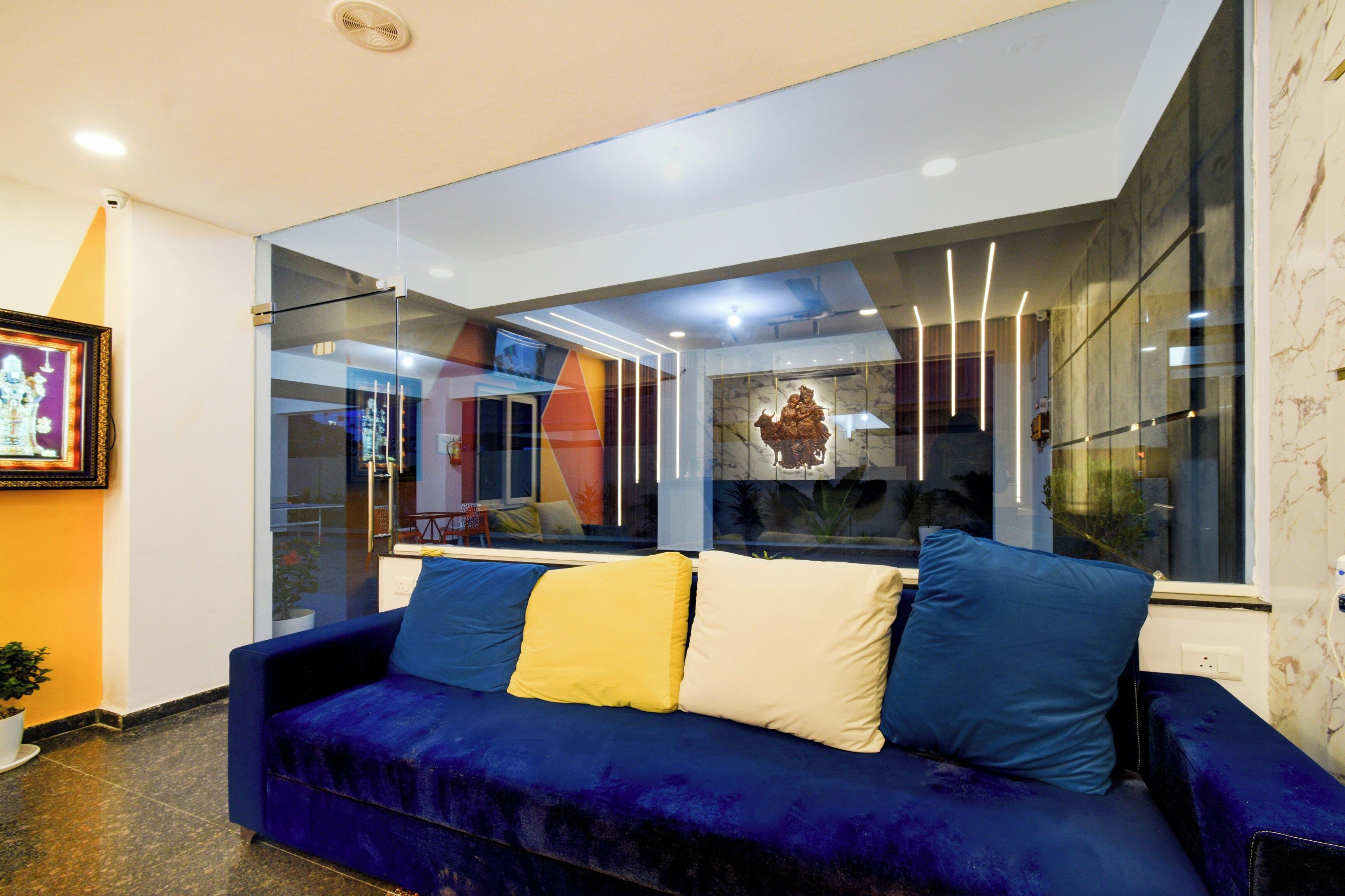 A modern living room with a blue sofa, a glass partition, and a view of the outside.