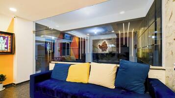 A modern living room with a blue sofa, a glass partition, and a view of the outside.