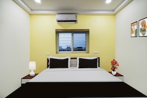 A hotel room with a bed, a window, an air conditioner, a nightstand, a lamp, and a vase with flowers. - Hotel O 4 COLORS (Hyderabad)