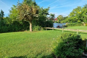 Een verzorgd gazon met houten omheining, een boom en een waterpartij in de verte.