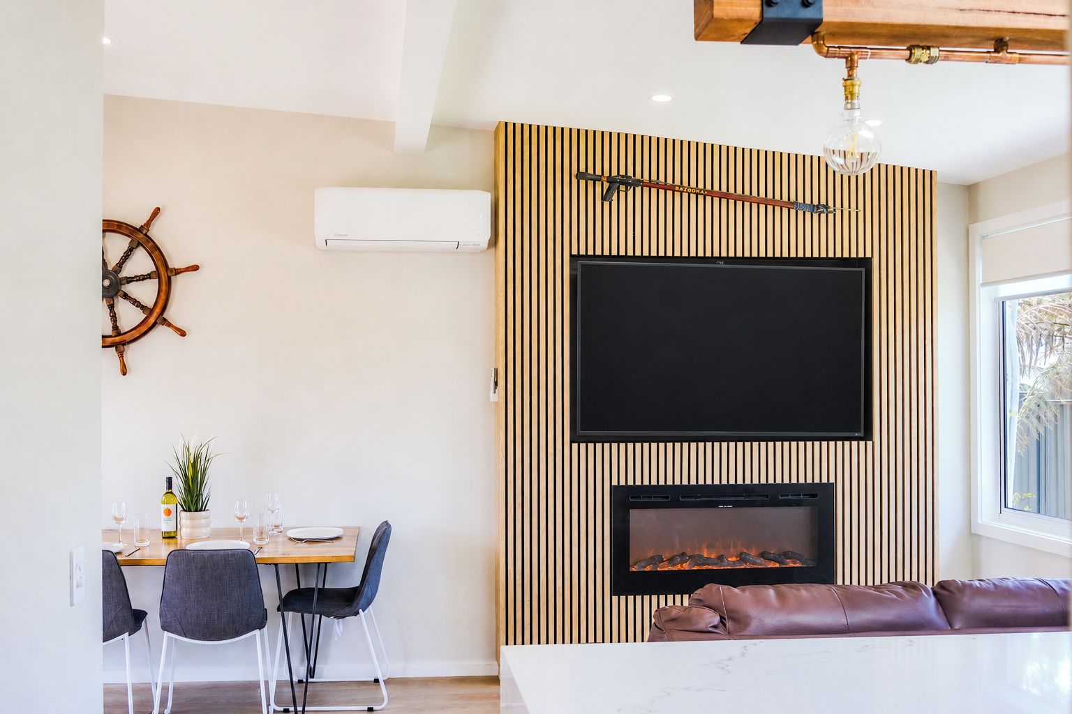A modern living room with a fireplace, a mounted television, and a dining area with chairs and a table.