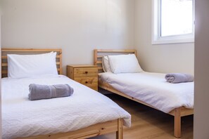 A room with two wooden beds, each with white bedding and pillows, a wooden nightstand, and a window providing natural light. - High-End Luxury Unit 8min Walk to Town & Cafes (Mallacoota)