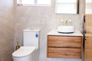 A bathroom with a toilet, a sink, and a wooden cabinet. - High-End Luxury Unit 8min Walk to Town & Cafes (Mallacoota)
