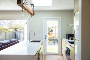 A modern kitchen with a large island, stainless steel appliances, and a view of the backyard. - High-End Luxury Unit 8min Walk to Town & Cafes (Mallacoota)