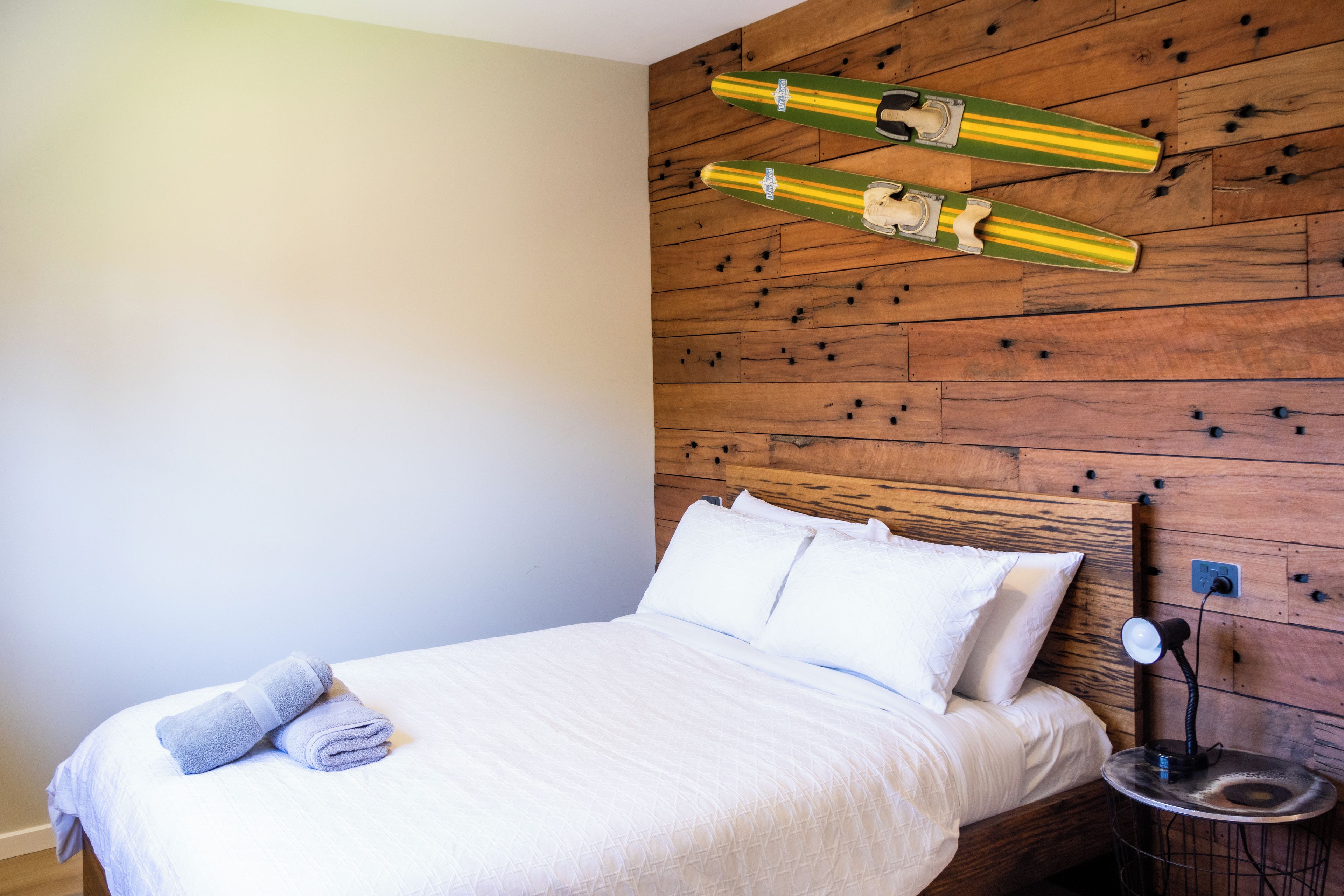 A bedroom with a wooden headboard, a bed with white bedding, and two skis mounted on the wall.