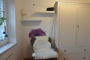 Una habitación con una silla blanca, un armario blanco y una estantería con una lámpara.
