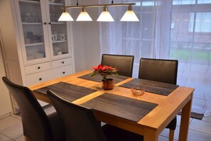 A dining table with four chairs, a vase with red flowers, and a glass of water. - Schürholz holiday apartment (Hooksiel)