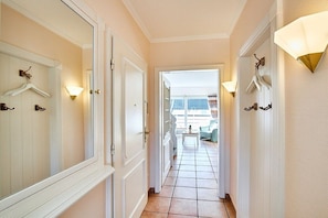 A hallway with doors, wall-mounted light fixtures, and a view into a room with a balcony. - Holiday apartment with 2 bedrooms (Wenningstedt)