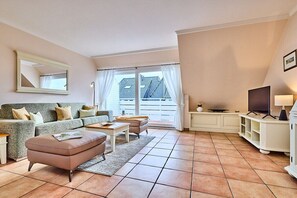 A living room with a sofa, ottoman, and a television on a stand. - Holiday apartment with 2 bedrooms (Wenningstedt)
