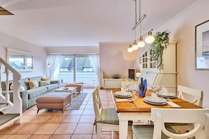 A modern living room with a sofa, ottoman, and dining table set for a meal. - Holiday apartment with 2 bedrooms (Wenningstedt)