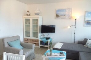 A living room with a television, a cabinet, a sofa, and a lamp. - Holiday apartment Strandidyll (Horumersiel)