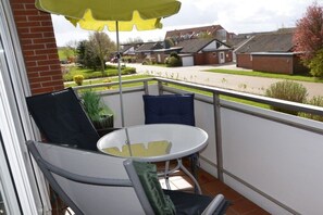 A balcony with a table and chairs, a yellow umbrella, and a view of a residential area. - Holiday apartment Strandidyll (Horumersiel)