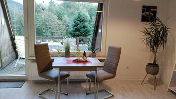 Un comedor con una mesa, sillas, una planta en maceta y vistas a un bosque a través de grandes ventanales.